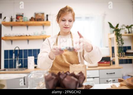 Jeune femme souriante avec tamis et muffins dans des tasses à pain avec sucre en poudre dans la cuisine de la maison Banque D'Images