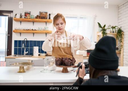 Jeune femme souriante avec tamis et muffins dans des tasses à pain avec sucre en poudre dans la cuisine de la maison Banque D'Images