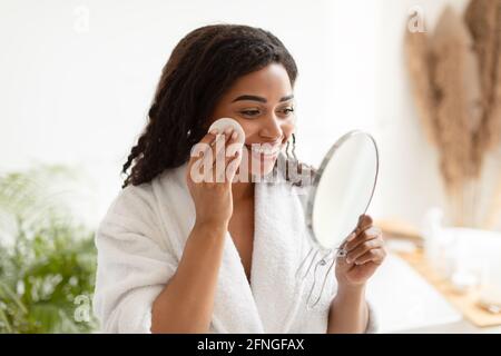 Femme noire utilisant un tampon de coton regardant le miroir dans la salle de bains Banque D'Images