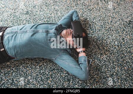Adult wearing casual clothes lying on the carpet experienced with virtual reality goggles. Banque D'Images