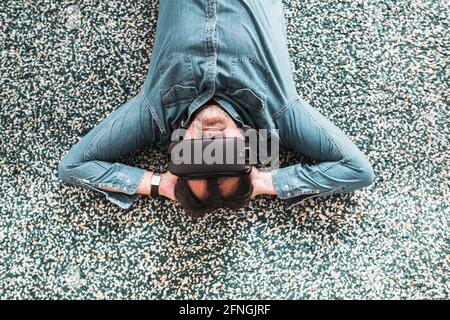 Adult wearing casual clothes lying on the carpet experienced with virtual reality goggles. Banque D'Images