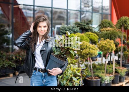 Une jeune jolie fille, vêtue d'une veste en cuir et d'un Jean, se tient près du centre de la fleur et tient un grand beau pot de fleurs Banque D'Images