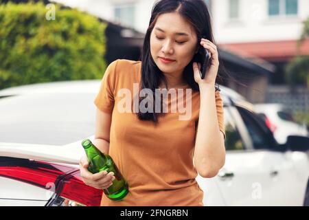 Femme tenant un téléphone portable et une bouteille de bière en voiture. Ne buvez pas et ne conduisez pas Banque D'Images