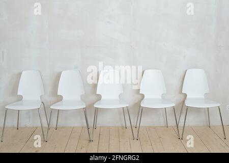 Rangée de chaises en plastique blanc sur pieds métalliques parquet contre mur gris Banque D'Images