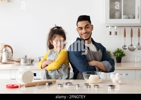 Petite fille mignonne et son papa arabe en tabliers posant Dans la cuisine Banque D'Images