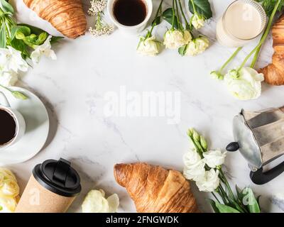 Cadre plat de préparation de tasses de café, de fleurs et de croissants sur fond de marbre. Concept petit déjeuner français. Vue de dessus. Copier l'espace Banque D'Images
