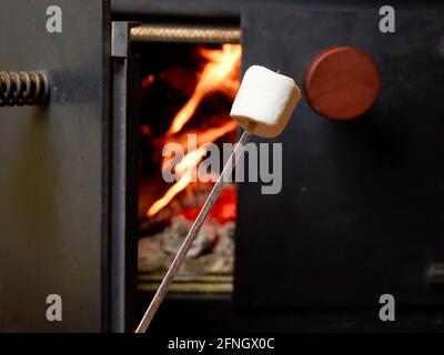 Guimauve sur brochette en métal devant les flammes d'époque cheminée en métal noir Banque D'Images