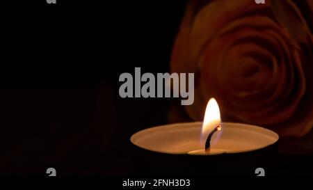 Gros plan d'une bougie de lumière de thé allumée avec une flamme brillante douce et rose floue dans un fond sombre Banque D'Images
