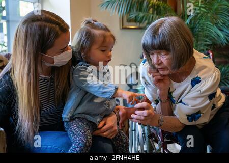 RETRANSMETTANT L'ORTHOGRAPHE DU NOM DE MIA À MYA LÉGENDE CORRECTE CI-DESSOUS Pat Tinner 79 (à droite) rencontre sa petite-fille Kimberley Skelton et sa grande petite-fille Mya (18 mois) pour la première fois depuis Noël à la maison de soins Sunrise of Bagshot à Bagshot, Surrey, les règles de verrouillage du coronavirus sont assouplies pour les résidents des foyers de soins. À partir de lundi, les résidents peuvent avoir jusqu'à cinq visiteurs désignés et peuvent aller sur plus de visites sans avoir besoin de s'isoler par la suite. Date de la photo: Lundi 17 mai 2021. Banque D'Images