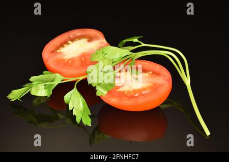 Deux moitiés d'une tomate rouge avec persil vert, gros plan, sur fond noir. Banque D'Images