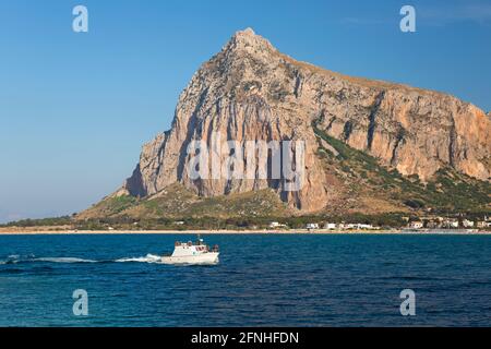 San Vito Lo Capo, Trapani, Sicile, Italie. Vue sur la baie jusqu'à l'imposante face nord de Monte Monaco, petit bateau retournant au port. Banque D'Images