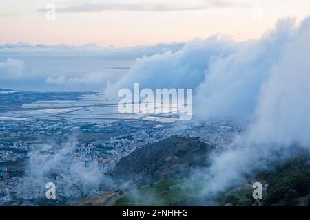 Erice, Trapani, Sicile, Italie. Vue sur les plats salins de Trapani depuis le sommet de Monte Erice, le crépuscule, les nuages bas s'écoulent à travers la colline. Banque D'Images