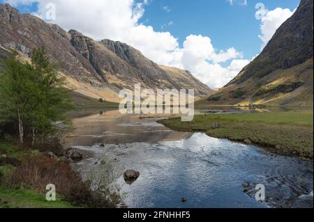 Paysage de Glencoe dans les Highlands écossais avec des reflets dans l'eau du loch, montagnes dont Aonach Eagach crête à gauche. Ciel bleu et nuages. Banque D'Images