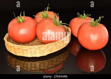 Plusieurs tomates roses juteuses dans une assiette de paille, gros plan, sur fond noir. Banque D'Images