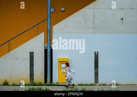 Une petite fille passe rapidement devant une boîte aux lettres publique jaune du Deutsche Post, qui se tient devant un mur de maison avec un escalier. Banque D'Images