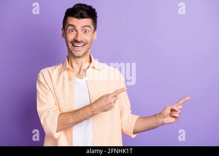 Photo de jeune homme promoteur indique l'usure de l'espace vide des index chemise beige isolée couleur violet arrière-plan Banque D'Images