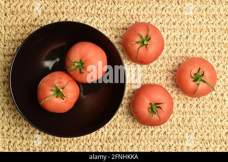 Plusieurs tomates roses juteuses dans une plaque en céramique sur un tapis de paille, vue rapprochée, vue de dessus. Banque D'Images