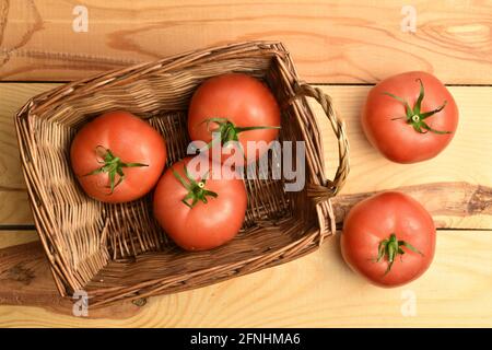 Plusieurs tomates roses mûres dans un panier, gros plan, sur une table en bois, vue de dessus. Banque D'Images