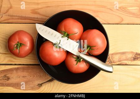 Plusieurs tomates roses juteuses dans une assiette avec un couteau, gros plan, sur une table en bois, vue de dessus. Banque D'Images