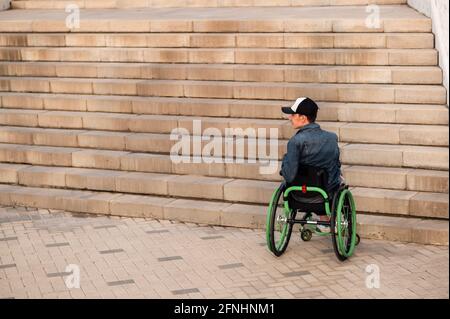 un jeune handicapé en fauteuil roulant ne peut pas entrer dans les escaliers. Environnement accessible pour les personnes handicapées Banque D'Images