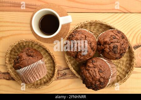 Plusieurs délicieux muffins au chocolat sur des assiettes en paille et une tasse de café, gros plan, sur une table en bois, vue du dessus. Banque D'Images