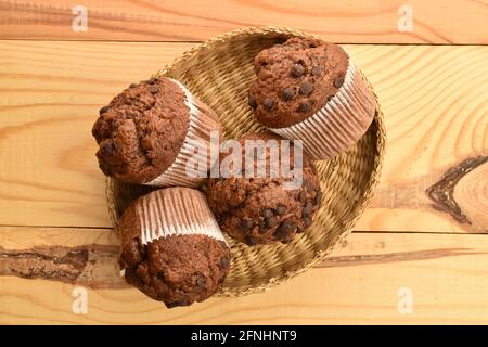 Plusieurs délicieux muffins au chocolat sur une assiette de paille, gros plan, sur une table en bois, vue de dessus. Banque D'Images