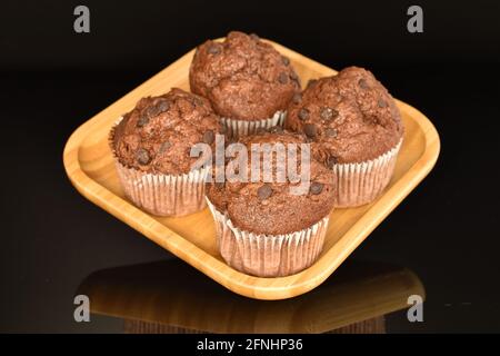 Quelques muffins au chocolat sur une assiette de bambou, gros plan, sur fond noir. Banque D'Images