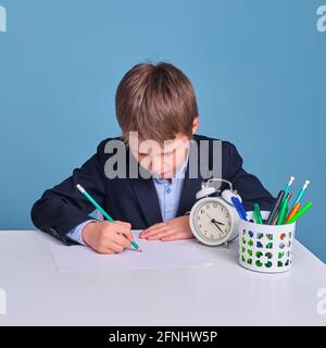 L'élève junior tire sur une feuille de papier à un bureau d'école, fond bleu Banque D'Images