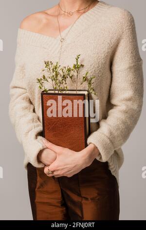 vue rognée d'une jeune femme tenant un livre avec des fleurs sauvages isolées en gris Banque D'Images