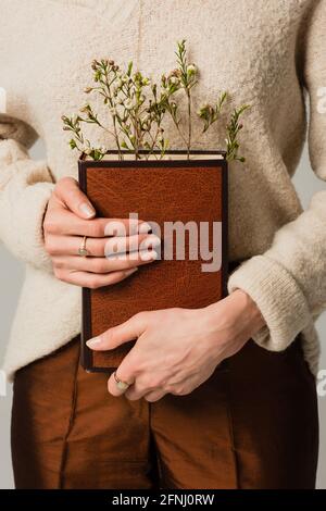 vue partielle de la jeune femme tenant un livre avec des fleurs sauvages Banque D'Images