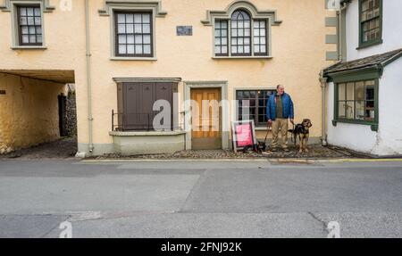 Homme avec ses deux chiens d'animal de compagnie attendant à l'extérieur du musée Beatrix Potter fermé à Hawkshead, Cumbria, Angleterre. Banque D'Images