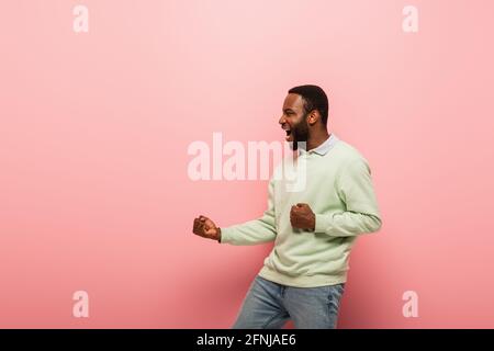 Vue latérale d'un homme afro-américain en colère avec les mains à l'intérieur poings sur fond rose Banque D'Images