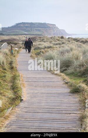 Deux personnes marchant sur UNE promenade en bois à travers Sand Dunes avec Warren Hill, Hengistbury Head in the Background, hiver Royaume-Uni Banque D'Images