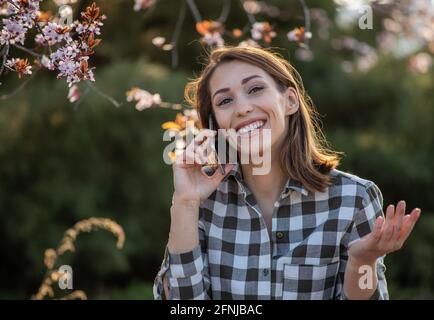 Une jeune femme heureuse qui parle sur un téléphone portable devant arbre fruitier en fleurs au printemps Banque D'Images