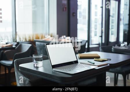 Ordinateur portable moderne avec écran blanc, verre d'eau et organiseur avec stylo sur table dans le café, concept de lieu de travail indépendant Banque D'Images