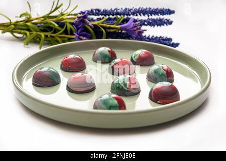 Bonbons au chocolat trempé à la main de collection avec un corps peint brillant sur une plaque ronde avec un fond flou et des éléments bokeh. Stock photog Banque D'Images