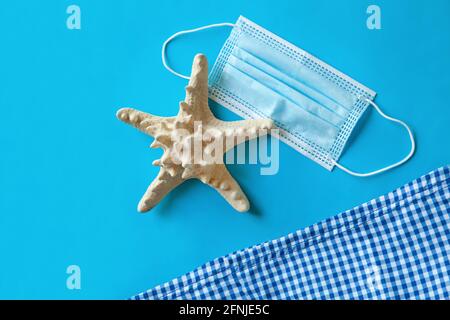 Masque médical près de la serviette de plage et de l'étoile de mer sur fond bleu, vue du dessus, articles de plage et concept d'été Banque D'Images