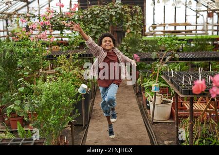 Petit garçon africain courant parmi les plantes et jouant dans le serre Banque D'Images