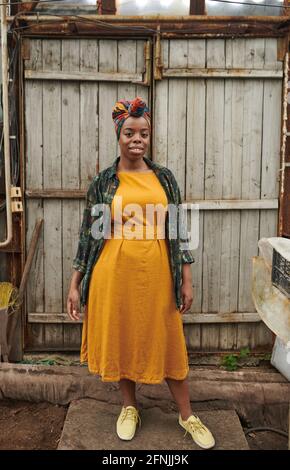 Portrait de la jeune femme africaine en belle robe jaune souriant à l'appareil photo lorsque vous êtes debout à l'extérieur Banque D'Images