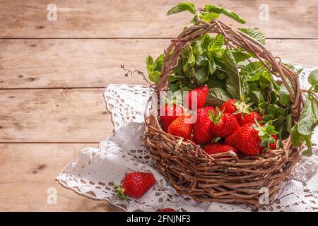 Panier en osier de fraises mûres. Baies fraîches, menthe aromatique. Ancienne table en bois, serviette en papier de style rustique, espace de copie Banque D'Images