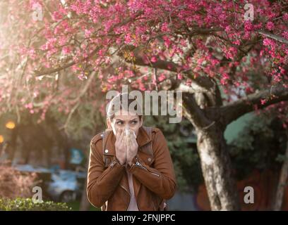 Jeune jolie fille soufflant le nez devant l'arbre en fleur. Réaction allergique printanière Banque D'Images