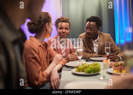 Groupe diversifié de jeunes qui discutent à table tout en appréciant dîner entre amis Banque D'Images