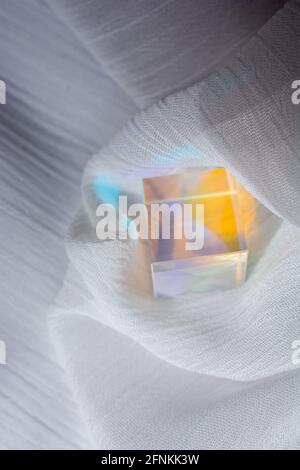 Cube en verre avec rayons à spectre de couleurs sur tissu. Arrière-plan abstrait avec réflexion et réfraction de la lumière. Banque D'Images