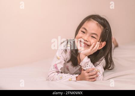 Enfant souriant fille couché sur le lit avec la main sur le menton, regardant à côté de l'image, espace pour la copie, couleur chaude. Banque D'Images