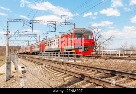 Un train électrique circule sur des voies ferrées rouillées contre un ciel bleu avec nuages blancs Banque D'Images