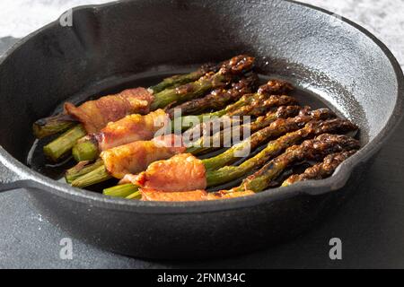 Asperges enrobées de bacon cuit dans une poêle en fonte. Sur une planche à découper en ardoise Banque D'Images