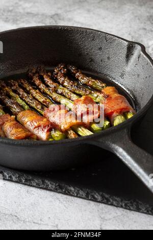 Asperges enrobées de bacon cuit dans une poêle en fonte. Sur une planche à découper en ardoise Banque D'Images