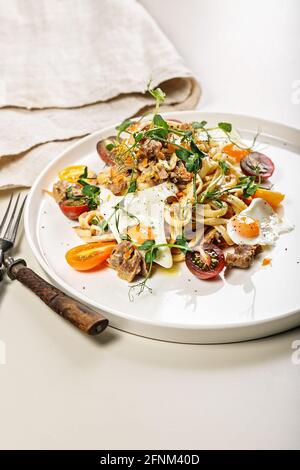 Gros plan de délicieux spaghetti faits maison avec légumes, fromage et œufs de caille frits sur une assiette ronde sur un fond clair. Cuisine italienne traditionnelle Banque D'Images