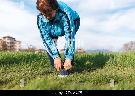 Une femme âgée règle ses chaussures de sport sur son pied tout en se tenant debout sur l'herbe. Douleur dans les pieds. Le concept d'un mode de vie actif et d'un problème de santé Banque D'Images