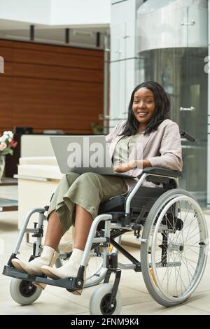 Femme africaine handicapée en fauteuil roulant utilisant un ordinateur portable pour le travail en ligne au bureau Banque D'Images